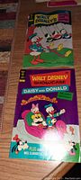 Two Walt Disney Donald Duck comics with bright cover illustrations laid flat on a wooden surface