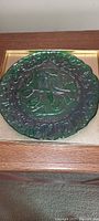 Top view of the green embossed glass plate showing detailed bird and foliage design in the center with scalloped edge embossed border.