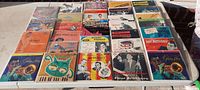 Thirty 45 RPM jazz vinyl records arranged in five rows of six on a tray, showing colorful cardboard sleeves with varied artistic designs and artist portraits.