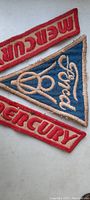 Three vintage sewn patches: one blue Ford triangular patch and two red Mercury rectangular patches.