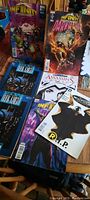 Photo showing 5 comic books on a wooden surface featuring Infinity, Dark Knight, Batman, and Assassin's Creed themes.