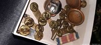 Close-up photo of various military uniform pins, buttons, and badges including multiple small brass buttons with '10' insignia, collar pins, and ribbon bar.