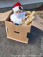 Front view with Santa Claus partially out of box showing head and white beard with red hat decorated with holly, glasses visible.