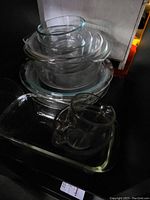 Stack of round glass mixing bowls and rectangular baking dishes, including a glass measuring cup with handle and spout, all clear glass.