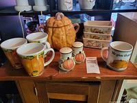 Full lot showing ceramic pumpkin cookie jar, harvest mugs, pumpkin-themed salt and pepper shakers, and small loaf pans.