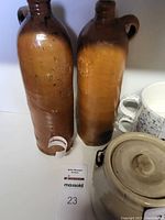 Two tall vintage stoneware jugs side by side, showing their brown glazed surfaces and handles by the neck.