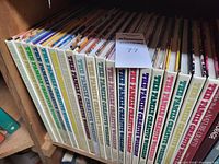 Spine view of 21 books in the series visible on wooden bookshelf, showing title 'The Family Creative Workshop' in multicolor lettering.
