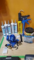Full lot on table showing caulking tubes, caulking guns, blue ratchet straps, and bungee cord pack