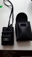 Black Bushnell 8x25 binoculars next to its black carrying case on a white surface, showing full item set.