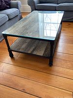 Front-left angle showing glass top, wood shelf and metal frame on wood floor