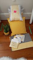 Four toss cushions and two faux plants arranged on floor with napkins and placemats in front.