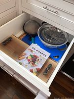 Drawer open showing assortment of cutting boards, strainers, and book titled 'On Boards'