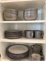 Stoneware Distinctly Home dinnerware set including bowls, plates, and mugs arranged on shelves