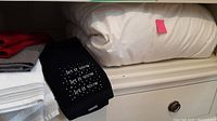 Folded white queen size down duvet on a shelf alongside folded towels including a black towel with white text and dots