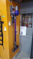 Full-length view of Dyson V6 vacuum mounted on wall bracket with manual visible below