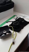 Ear pods inside charging case with yellow USB charging cable beside it and Lifetrons wireless speakers on black cloth pouch in the background.