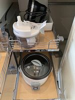 Overview photo showing three kitchen appliances on slide-out shelf: KitchenAid hand mixer at back, Starfrit chopper in middle, Black & Decker cooker at front