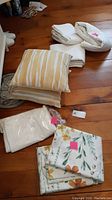 Overview on hardwood floor of floral duvet cover and shams, striped toss cushions, and folded white linens