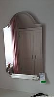Photo of wall mirror showing scalloped edges and part of room reflection including door and bathtub.