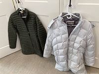 Photo showing both jackets hanging, including the silver Eddie Bauer jacket with hood and the olive Travex jacket behind it.