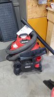 Shop-Vac wet/dry vacuum showing red and black unit with hose wrapped around and manual on top.
