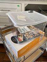 Plastic sous vide water container with a lid placed on its original packaging box on a kitchen cart.