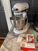 Front view of white KitchenAid Classic mixer with bowl and manual on countertop