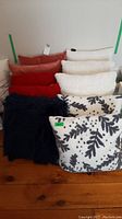 Front angled view showing the arrangement of ten toss cushions in various fabrics and colors on a wooden floor.