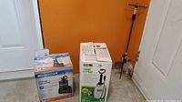 Mastercraft utility pump and boxed Home Gardener stand and spray sprayer beside a metal lawn sprinkler leaning against wall.