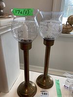 Pair of brass candle holders showing full height with etched glass shades and candle inside.