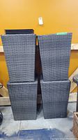 Four gray resin wicker square planters stacked in two columns against a yellow wall