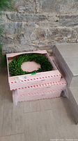 Three preserved boxwood wreaths stacked in branded Jillian Harris & Crate & Barrel boxes against a stone wall.