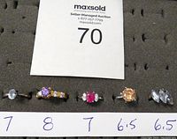 Full overview shot of five rings arranged in foam with size markings 7, 8, 7, 6.5, 6.5 and a MaxSold auction card.