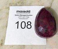 Front view of large faceted pear-shaped ruby with auction lot number 108 card as background