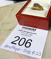 Gold-tone ring with oval amethyst placed in a red jewelry box, photographed with auction lot number 206 tag.