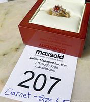 Ring in jewelry box with auction lot number 207 and handwritten note Garnet size 6