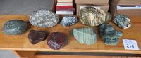 Wide view of all nine polished and natural geological rocks arranged on a wooden bench showing varied colors and textures.