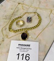 Full view of the jewelry items including gold chain necklace with dark purple pendant, gold-tone ring with clear stones, silver-tone ring with multi-colored stone.