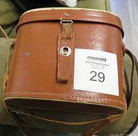 Closed brown leather carry case with shoulder strap for storing binoculars.