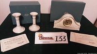 Photo showing the pair of Lenox candlesticks, mantel clock, original green Lenox boxes, and certificates of authenticity all arranged on a black surface.