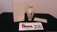 Photo showing the vase, original box and certificate of authenticity on display against a dark surface and off-white wall backdrop.