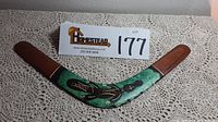 Top view of the curved boomerang painted with abstract Aboriginal style art on a green background, brown ends visible.
