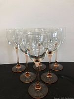 Six wine glasses grouped together on black surface showing all stems and bases with pink depression glass detail.