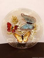 Front view of the round glass platter showing three colorful butterflies and foliage design on clear glass.