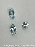 Photo showing three unmounted blue topaz gemstones with mixed cuts laid out on white background.
