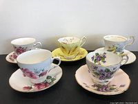 Lot of 5 tea cups and saucers showing floral decorative designs and gold trim.