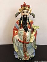 Front view of detailed porcelain Asian emperor statue with colorful robes, long beard, and ornamental staff.