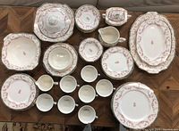 Overhead view of full dinner set including plates, bowls, cups, serving dishes, creamer, and covered sugar dish, all with pink rose floral pattern and gold-trimmed edges