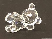 Full view of the clear Swarovski crystal bear figurine showing its faceted crystal body and black eyes on a black surface.
