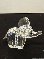 Clear Swarovski crystal elephant figurine showing faceted body and clear ears, trunk with black crystal eyes, placed on black surface.